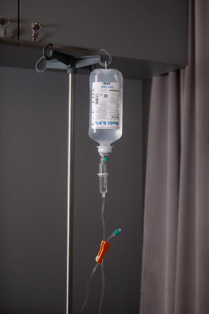 Infusionsflasche mit Kochsalzlösung an einem Infusionsständer in einem Behandlungsraum